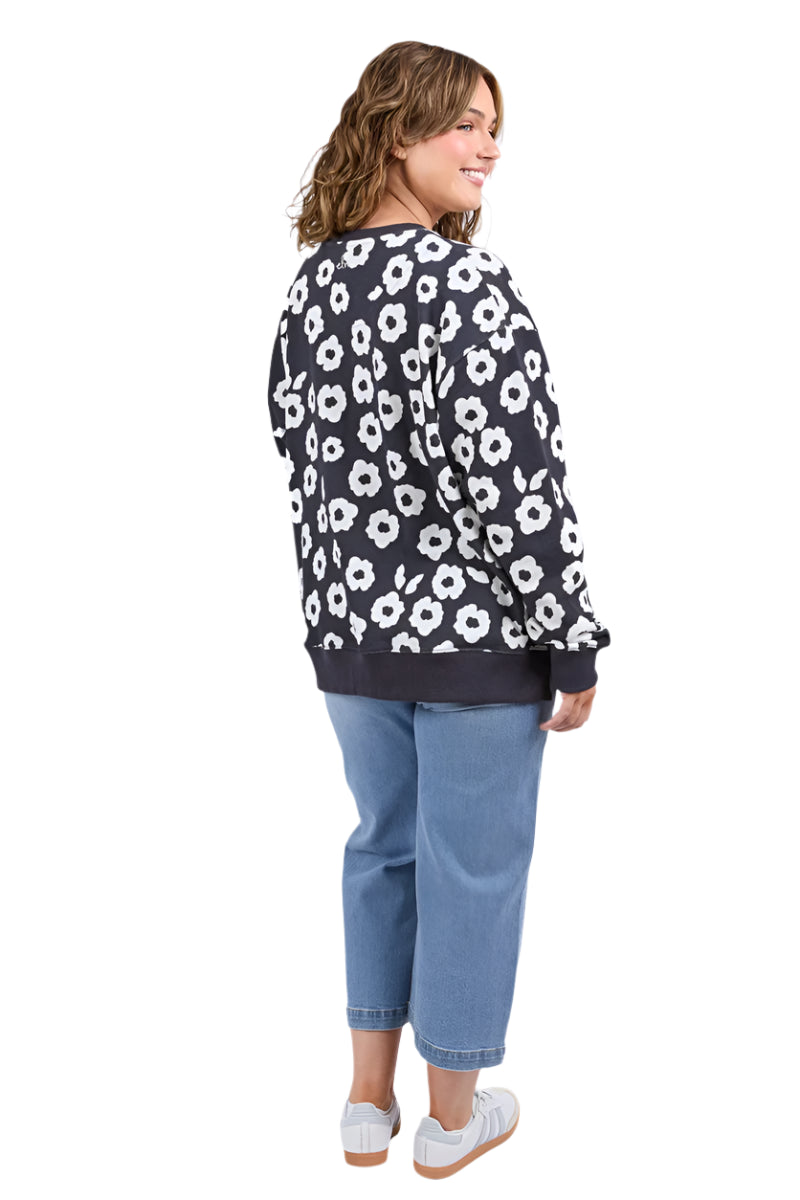 Woman wearing a navy sweater with white floral pattern and blue jeans on a white background