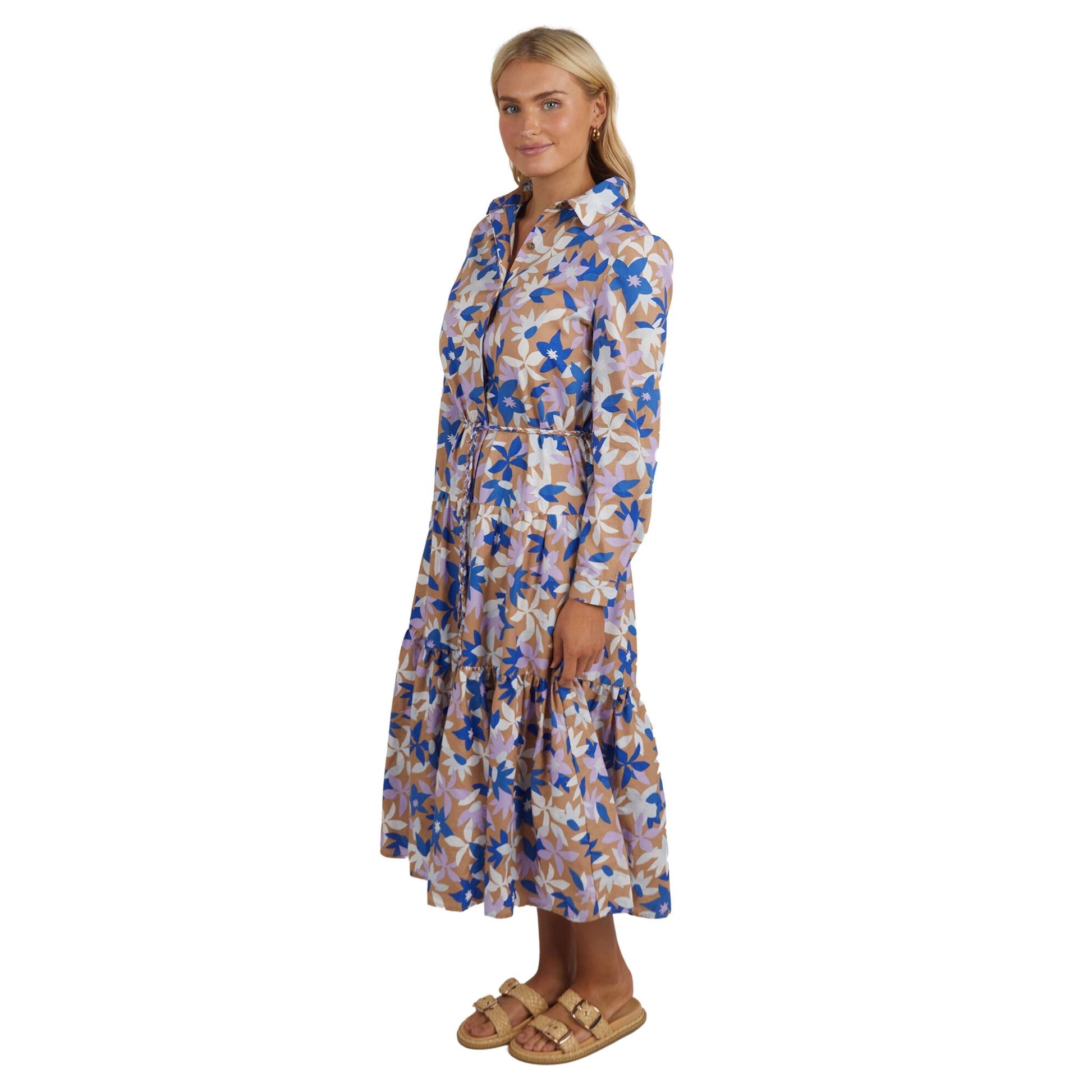 This pretty shirt style floral print dress features a button front and cuff and a cute collar. With a gently tiered skirt, hidden pockets, a self tie belt the Marguerite dress from Elm features blue and white abstract flowers on a coffee coloured base