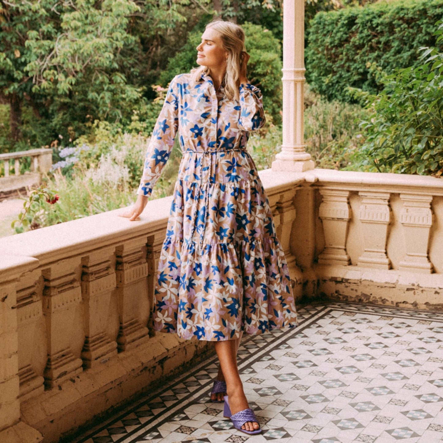 This pretty shirt style floral print dress features a button front and cuff and a cute collar. With a gently tiered skirt, hidden pockets, a self tie belt the Marguerite dress from Elm features blue and white abstract flowers on a coffee coloured base