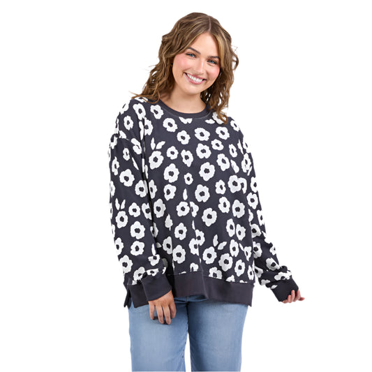 Woman wearing a navy sweater with white floral pattern and light blue jeans on a white background